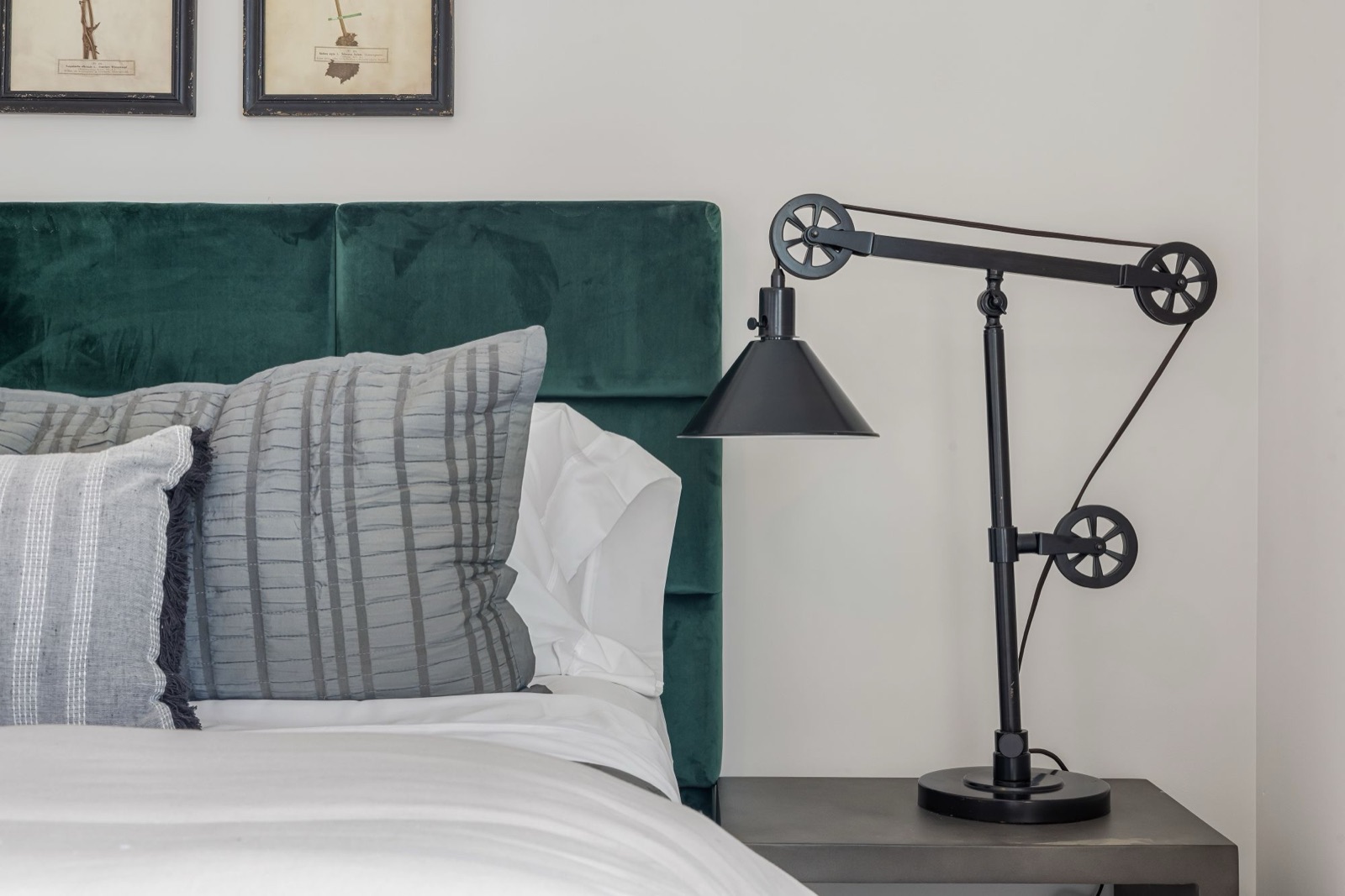 A green velvet headboard behind white bedding and striped pillows, with a black pulley lamp on the bedside table.
